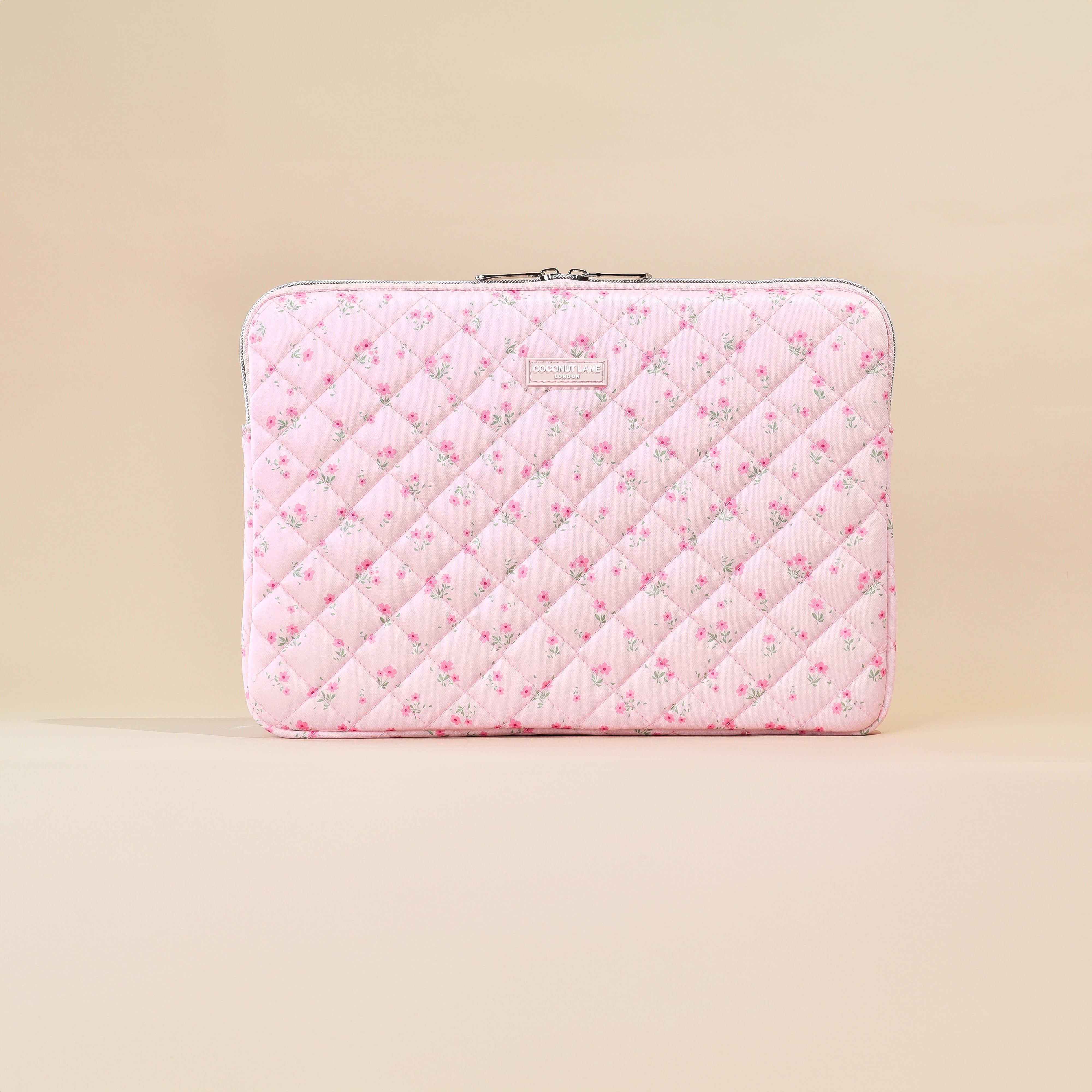 Pink quilted laptop sleeve with ditsy floral pattern on a beige background.