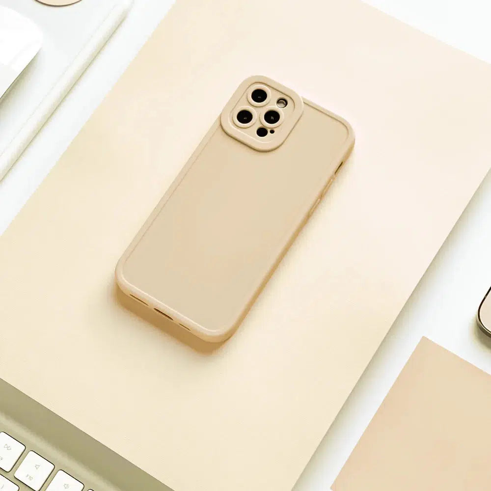 A smartphone with a beige case is placed on a light beige surface, surrounded by partially visible white objects including a keyboard and a piece of paper. The phone's camera setup is visible in the upper left corner.