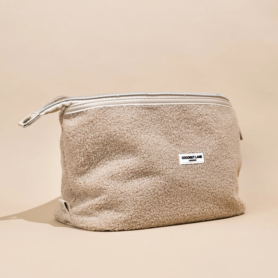 A beige, textured fabric pouch with a white zipper at the top and a small white label on the front that reads "COCONUT LANE". The background is a light, neutral color.