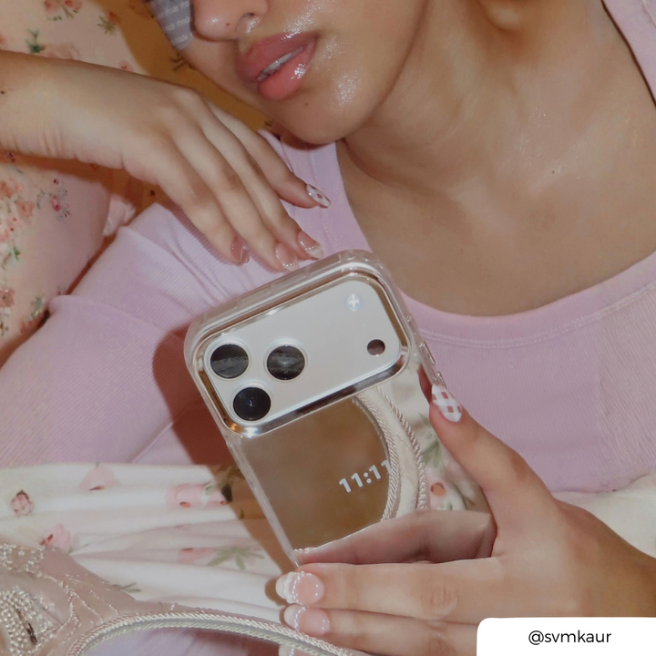 Woman in baby pink gown, holding an phone up to her ear. The phone is in a mirrored cases, with "11:11" text printed on the back. 