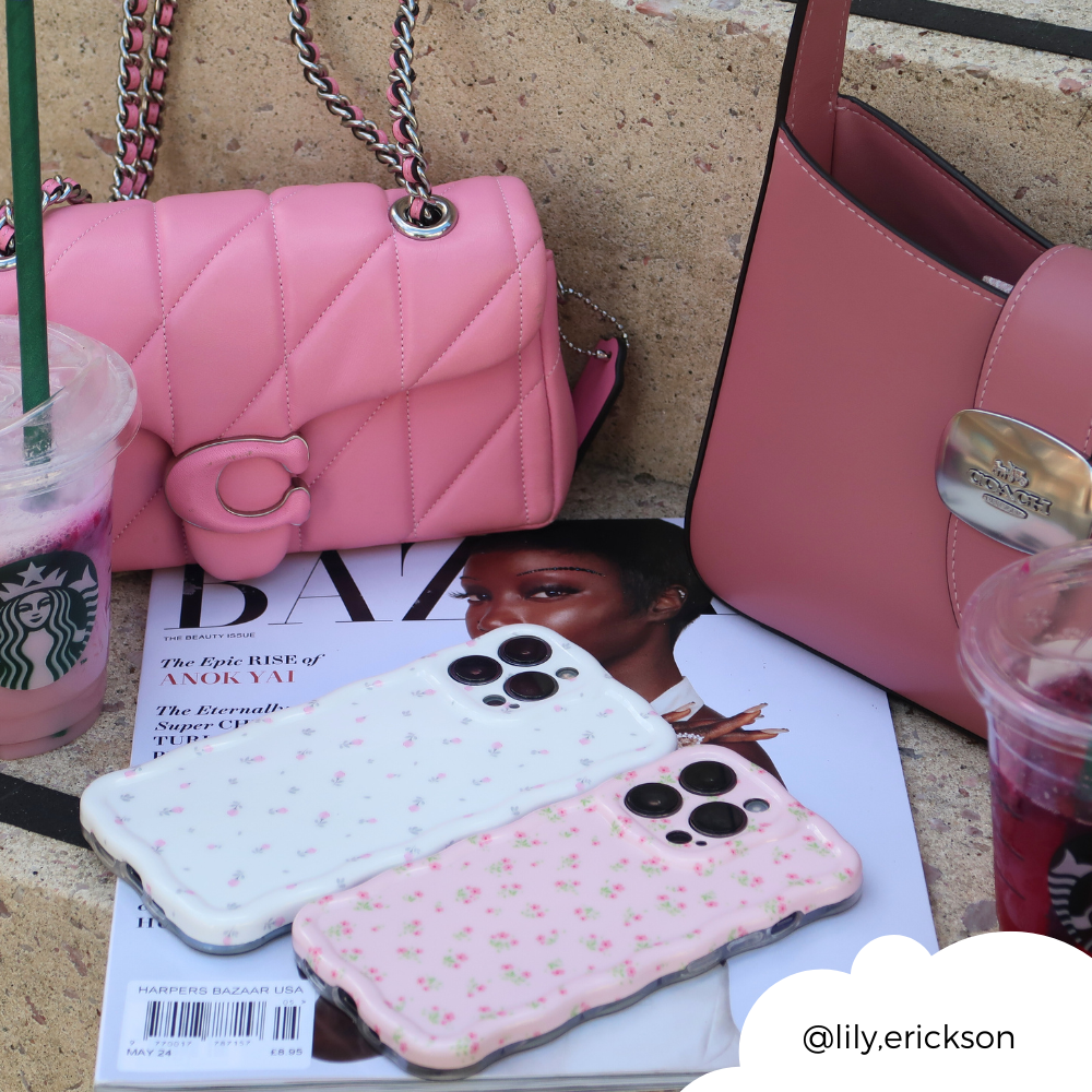 Two pink handbags and two Coconut Lane Wavy Phone Cases in Ditsy Floral White rest on top of a fashion magazine and a stone step. Beside them, there are two Starbucks drinks, one with a green straw and another with a purple hue. The Instagram tag "@lily.erickson" is visible.