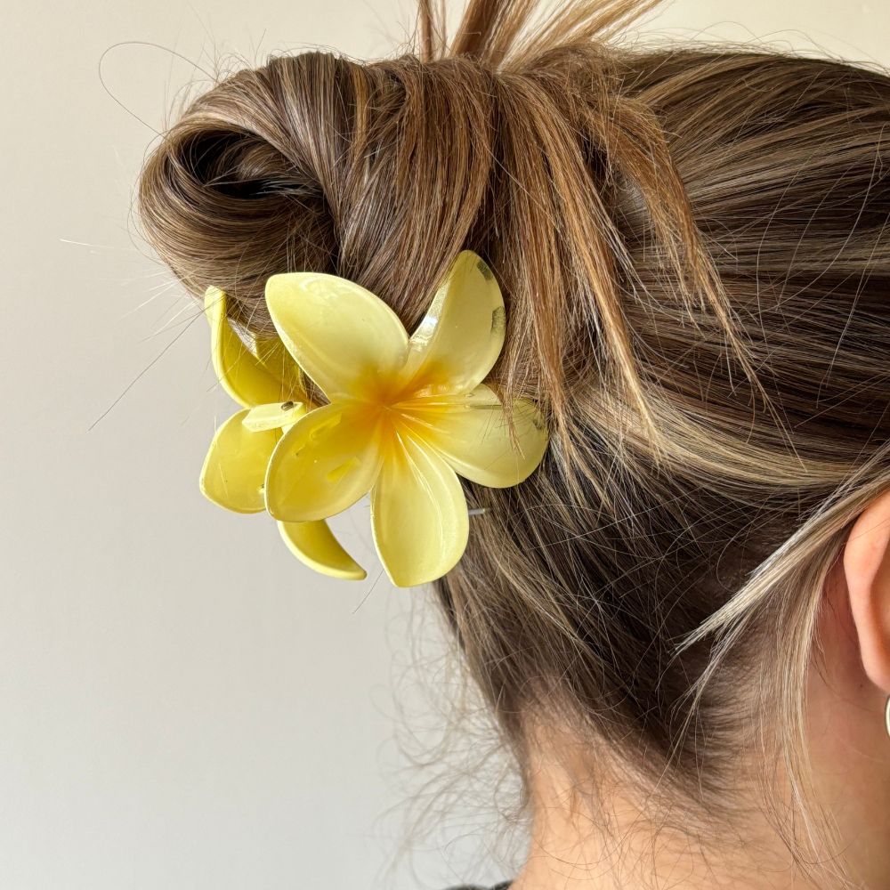Woman with a messy bun styled using a butter yellow tropical flower claw clip against a plain background.