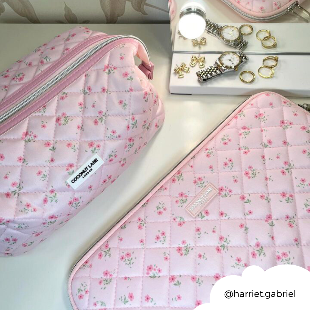 Pink quilted floral laptop sleeve on white surface with gold jewelry, watches, and a mirror nearby.