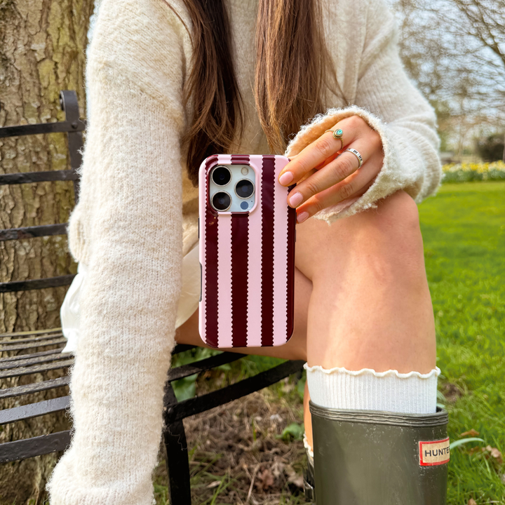 Girl sat in field with blushberry scallop stripes tough phone case in hand wearing cream outfit