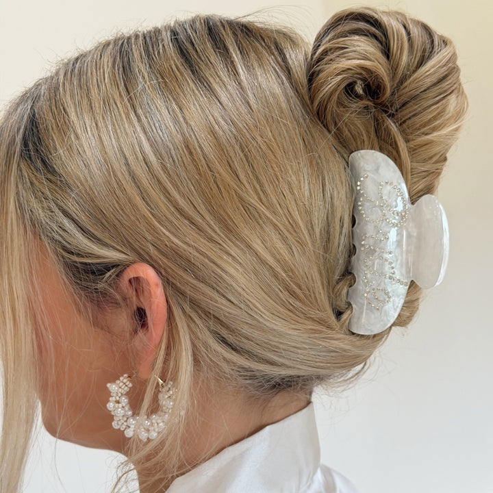 Blonde hair styled in an updo with a decorative bride claw clip on a plain background