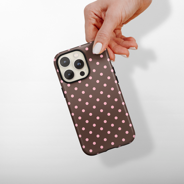 Hand holding a dual-layer phone case with brown polka dots and pink spots on a white background.