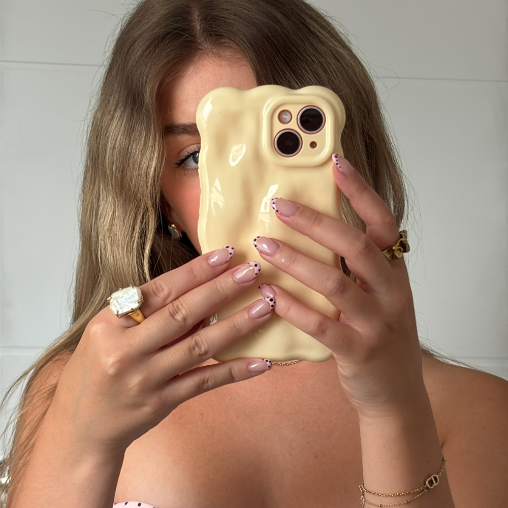 Woman with light brown hair holds a butter yellow 3D bubble phone case, displaying her manicure and a ring.
