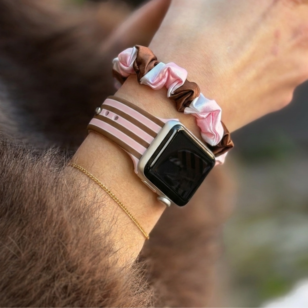 Pink and Brown stripes silicone sport band, attached to a black Apple Watch smartwatch on a woman's wrist alongside a matching cocoa and pink striped satin scrunchie.