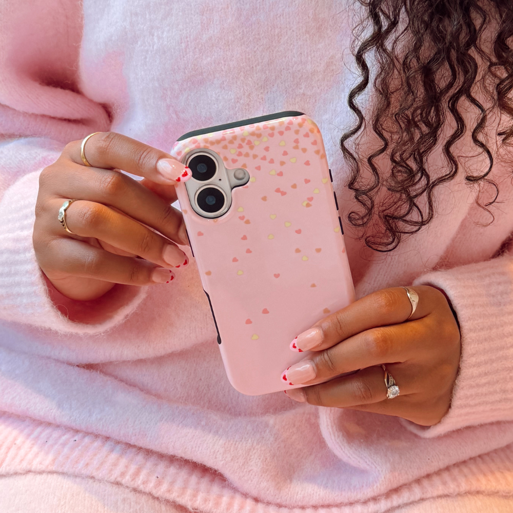 Person holding a pink phone with a heart pattern, wearing a pink sweater.