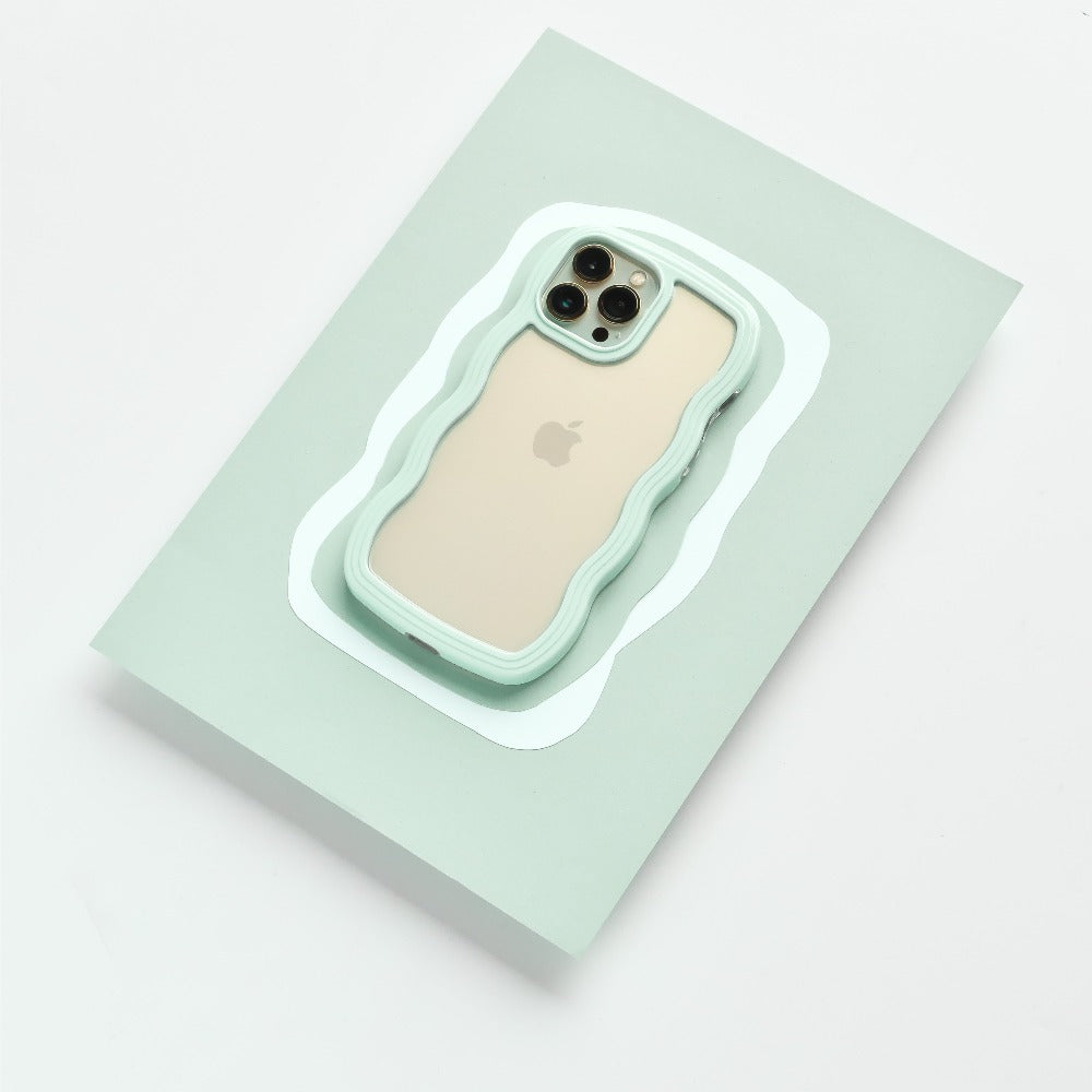 A gold iPhone, identified as an iPhone15, is encased in the rugged and wavy-edged Coconut Lane Curvy Phone Case in Mint. It's placed on a light green rectangular surface with a precise cutout that fits the phone perfectly. The camera lenses and Apple logo remain visible through the protective case.