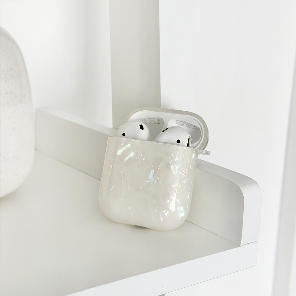 Iridescent pearl Coconut Lane Airpods case with white wireless earbuds on a white shelf against a minimal background.