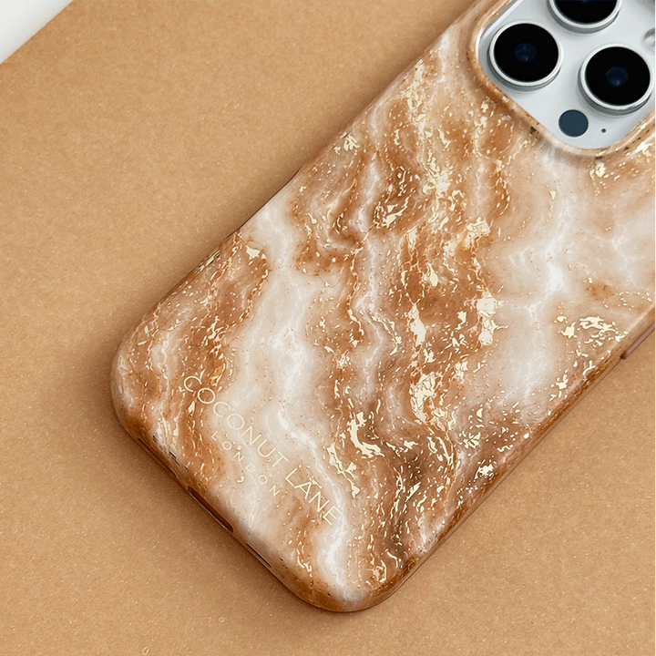 Cream and caramel marble phone case with gold veining, on a phone with three camera lenses, resting on a tan surface.