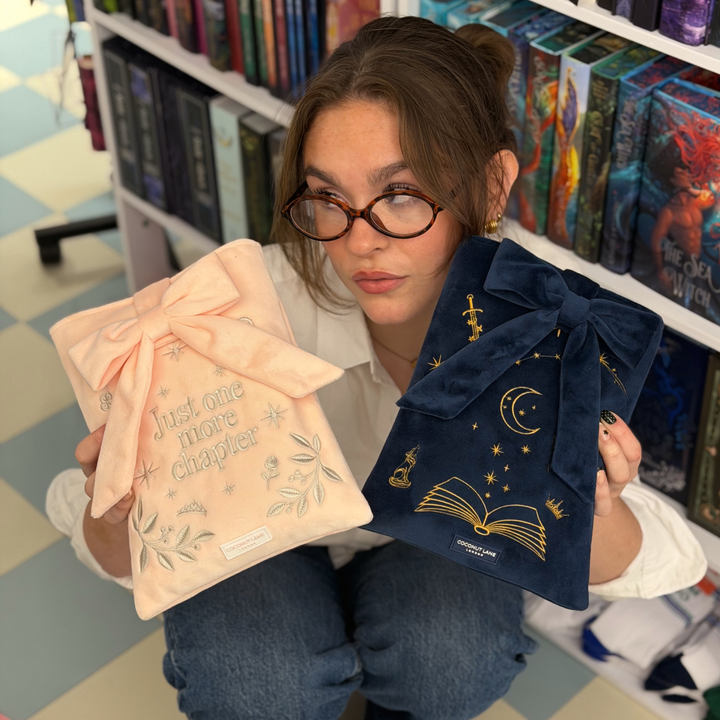 Book Sleeve made from soft blush pink velvet with grey embroidered floral details, stars and 'Just One More Chapter' lettering, finished with a large pink velvet bow and Coconut Lane logo, 