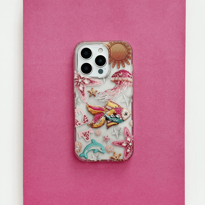 Clear phone case with pink accents, embroidered sea creatures, and sun design from Coconut Lane.