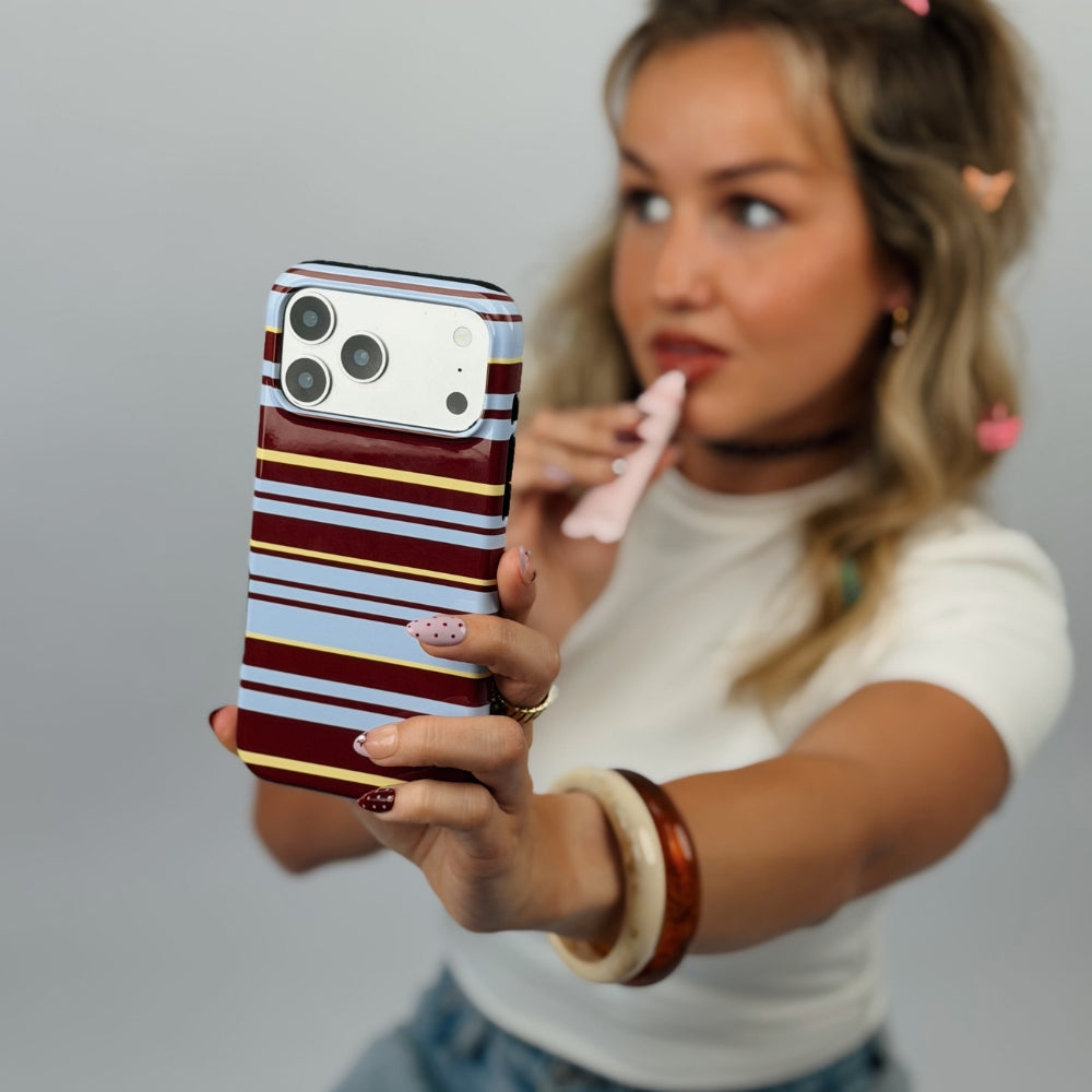 A woman holding a smartphone with Mary-Kate striped phone case featuring horizontal bands of brown, light blue, and yellow. 