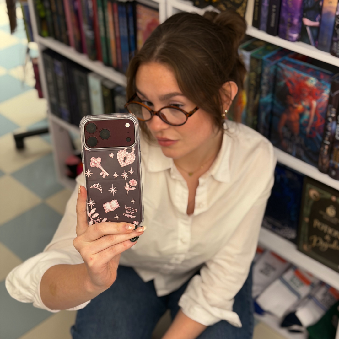 Woman in bookstore taking a selfie with a burgundy iphone. The iphone is in a Romance Girly Clear Phone Case showing intricate pink key, heart padlock, floral and star details with clear edges.