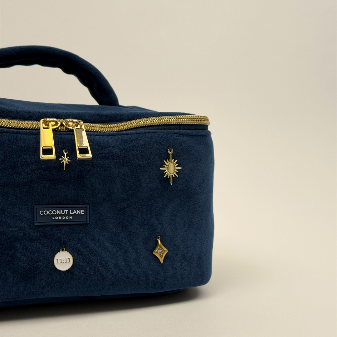 Stardust After Dark Vanity Case. A dark blue navy velvet vanity case with gold zip, and sewn-on gold celestial-themed charms. Including a moon, sun, star, diamond shape and 11:11 charm. 