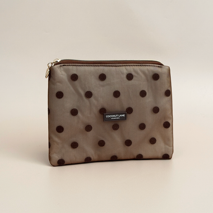 Brown mesh pouch with dark brown polka dots, a gold top zip with a heart-shaped zip pull, and a black Coconut Lane London logo badge on the front, shown on a beige background.