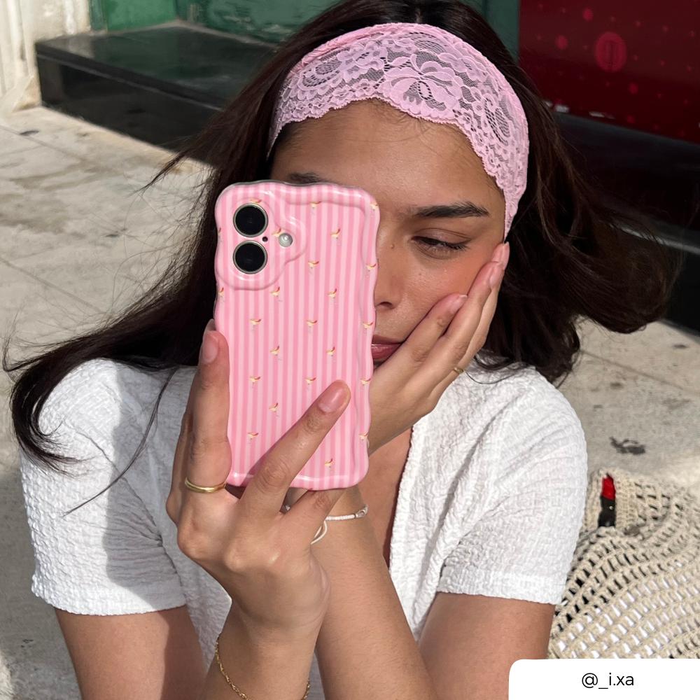 Girl with brunette hair wearing a pink lace hair band on her head, holding a wavy pink striped phone case with small spicy margarita illustrations.