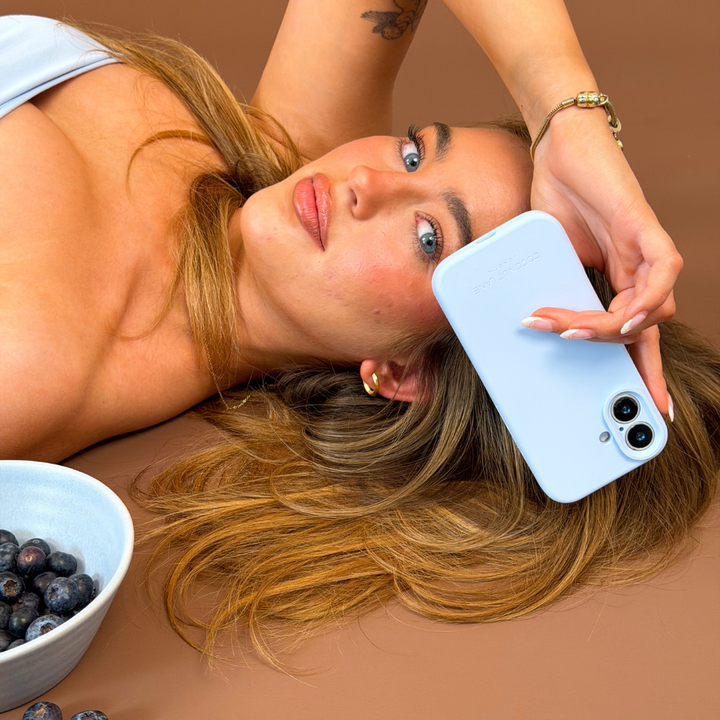 Girl holding butter soft silicone phone case in blue next to her face in a brown studio setting 