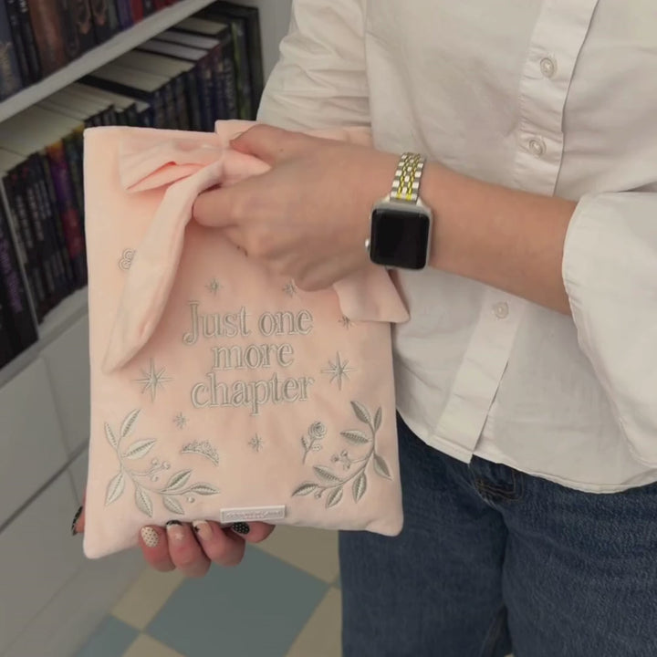 Book Sleeve made from soft blush pink velvet with grey embroidered floral details, stars and 'Just One More Chapter' lettering, finished with a large pink velvet bow and Coconut Lane logo, 