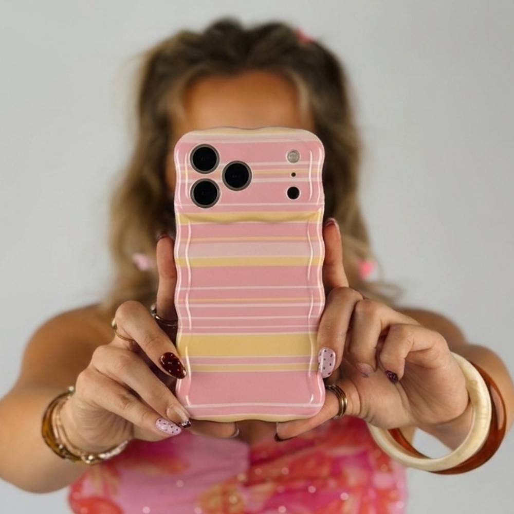 Woman holding a wavy retro ashley stripes phone case. The phone case has pink, yellow and white horizontal lines.